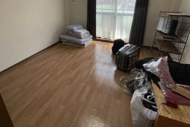 リゾートバイトの寮の部屋の画像。床はフローリングで、布団やスーツケースが置かれている。リゾートバイトの寮の部屋の画像。