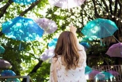 木々にカラフルな傘が吊るされた、おしゃれなカフェの風景の画像。女性が後ろ姿で、傘に手を伸ばしている。リゾートバイトの休日に観光を楽しんでいる様子が伝わってくる、風景の画像。