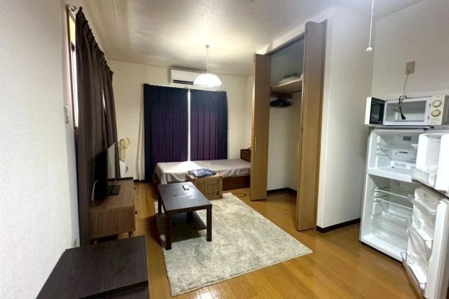 ベッド、テレビ、テーブル、ラグが完備された清潔感のあるリゾートバイトの完全個室寮の画像。クローゼットや冷蔵庫、電子レンジなどの家電も備え付けられた、快適な一人暮らし空間。