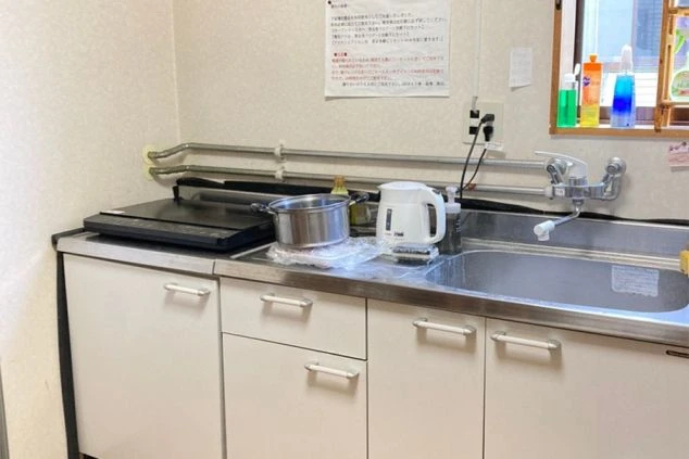 リゾートバイトの社員寮の共用キッチンのイメージ画像。IHクッキングヒーターとシンク、電気ケトルなどが写っている。