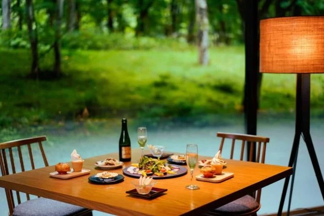 深い緑の森を背景にしたレストランのテーブルに置かれた洋食のコース料理の画像。