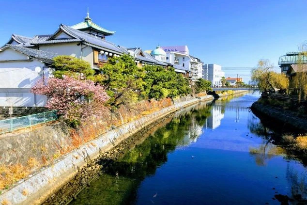  伊東温泉の松川沿いの風景。風情ある建物と青い川の流れ。リゾートバイトの休日に散策できる温泉地の美しい街並み。