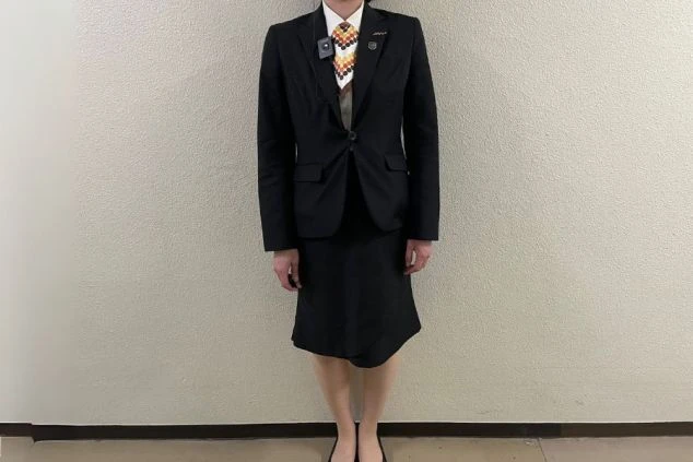 黒いスーツとスカート、白いシャツを着用した女性スタッフの画像。首にはオレンジ色のスカーフを巻いており、ホテルや旅館でのリゾートバイトの仕事内容を表す、フロントスタッフの制服の画像。