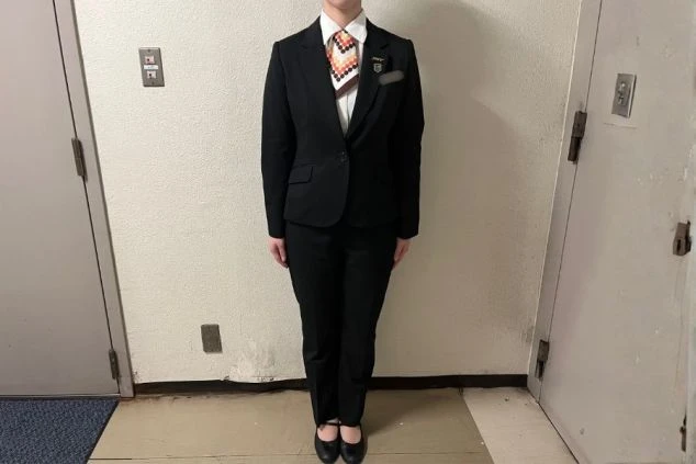 黒いスーツとパンツ、白シャツ、スカーフを着用した女性スタッフのベル・フロント・ドライバーの制服画像。