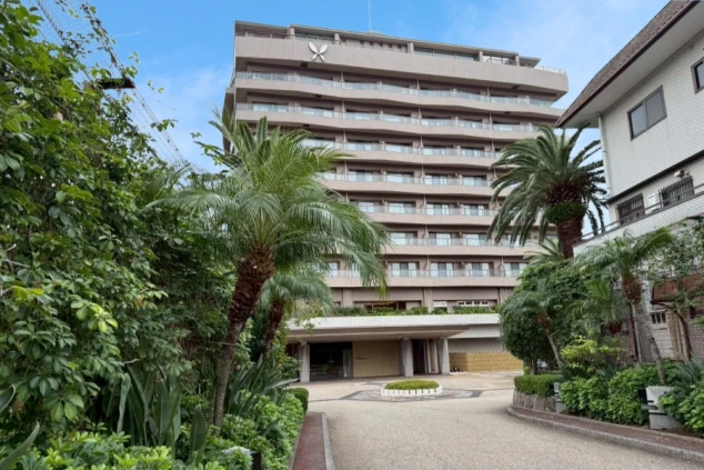 青空の下、大きなヤシの木に挟まれるように建つ、現代的な多層階の大型ホテルの外観。