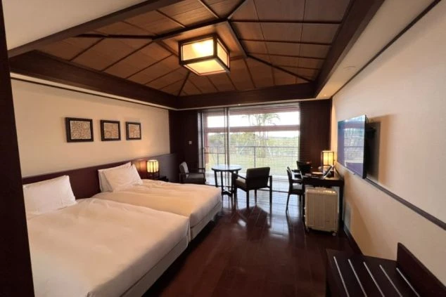 木製の格天井とフローリングが特徴的な、ツインベッドと窓際のテーブルセットがある洋室。