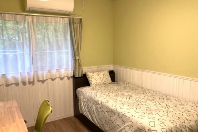 黄緑色の壁と白い羽目板の部屋。窓際にはデスクとアルファベット柄の寝具のシングルベッドがある。