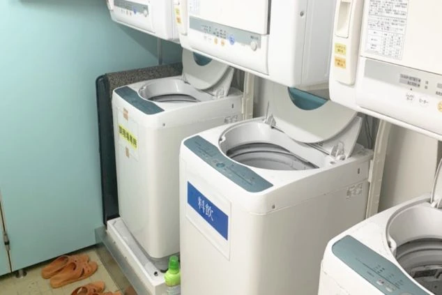 共用のランドリールームに並ぶ、2台の全自動洗濯機と上部に設置された衣類乾燥機。洗濯機には「調理場専用」「料飲」と用途別のラベルが貼られ、管理されている。