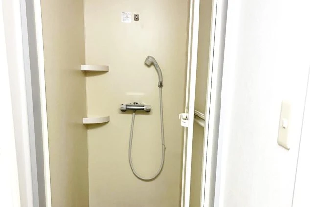 シンプルな個室内のシャワーブース。温度調節可能な混合水栓とシャワーヘッド、小物を置くための2段の棚が設置された、清潔感のあるコンパクトな設備。