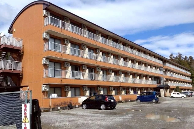 駐車場を完備した、窓が多く明るい雰囲気のマンションタイプの寮外観。