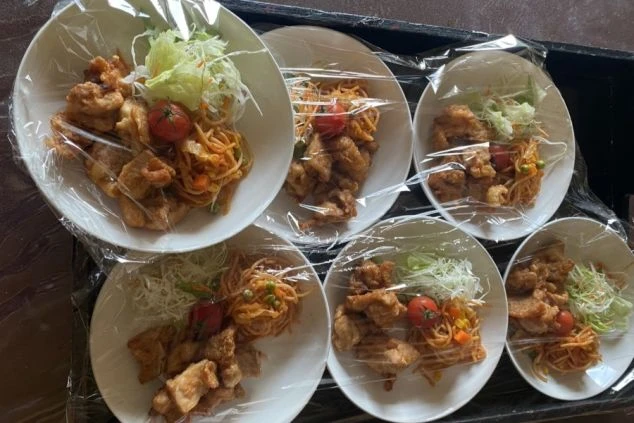 唐揚げとナポリタン風のパスタ、千切りキャベツとミニトマトが盛り付けられ、ラップがかけられている。