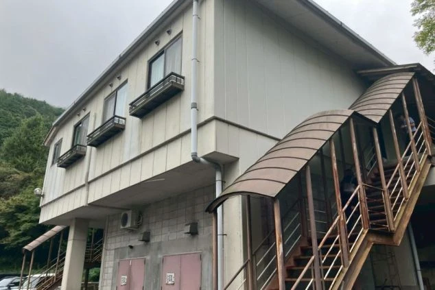 屋根付きの外階段が設置された、2階建ての白い寮の外観。