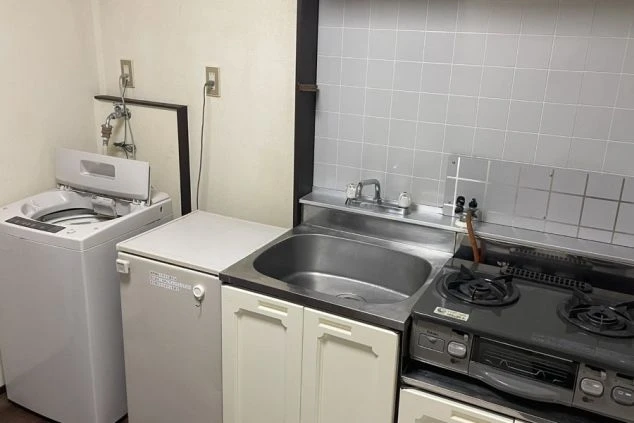 2口ガスコンロのキッチンと、その横に並んだ小型冷蔵庫、全自動洗濯機。