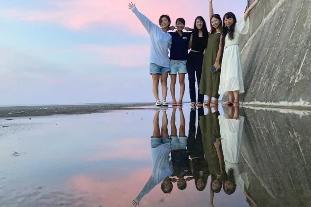 夕焼けのビーチでポーズをとるリゾートバイトの仲間たち。南国リゾートでの友達作り。