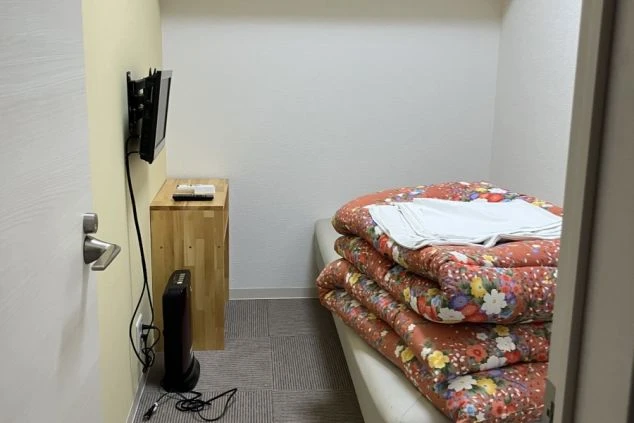 リゾートバイトの寮の部屋の中を撮影した画像。壁にはテレビが取り付けられ、ベッドの上には布団が畳んで置かれている。リゾートバイトの寮の部屋の画像。