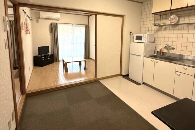 静岡県・伊豆市のリゾートバイトの寮のお部屋の画像。手前には冷蔵庫や電子レンジも完備したダイニングキッチンがり、奥にはリビングがある。