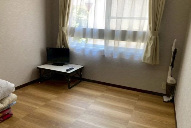 ワクトリの社員が出張で撮影した、リゾートバイトの寮個室の画像。フローリングで、部屋の端にはテレビと掃除機が置かれている。カーテンからは日光が差し込む。