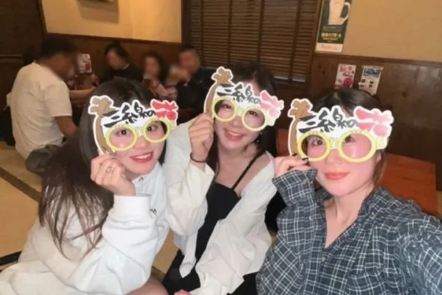 居酒屋で面白いメガネをかけて笑顔でポーズをとる3人の女性。リゾートバイトの仲間との楽しい時間。