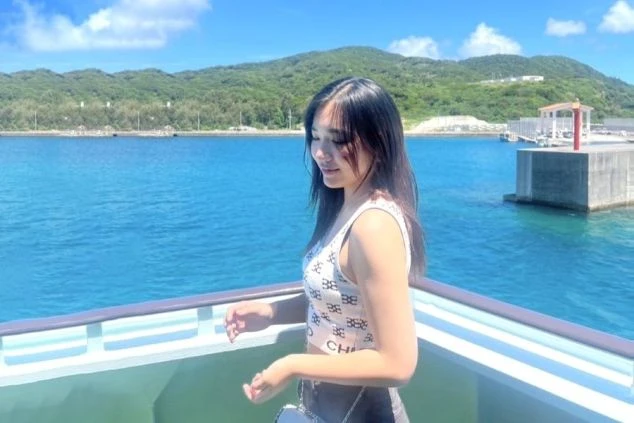 船上から青い海と緑豊かな島を眺める女性。リゾート地でのクルーズを楽しむ様子。