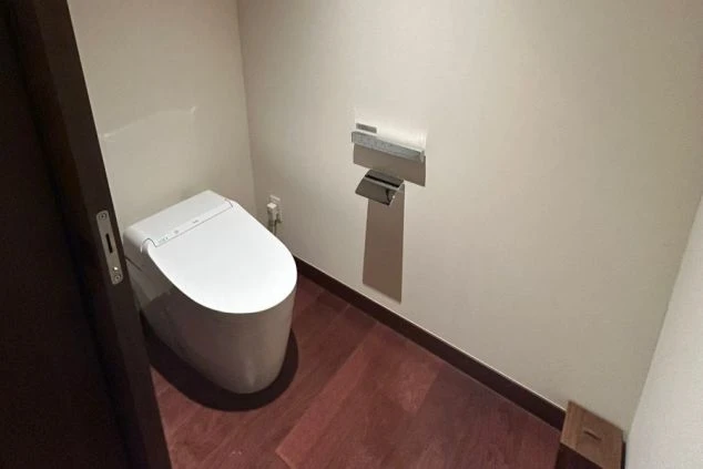 木目調の床と白い壁のシンプルな空間に、温水洗浄機能付きの洋式トイレ。