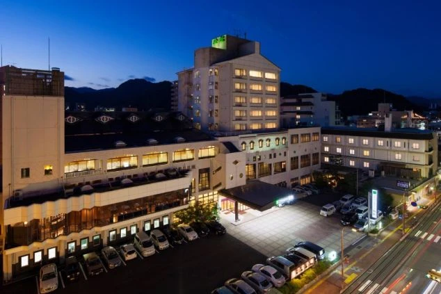 湯田温泉にあるホテルの夜の外観の画像。ライトアップされた建物が暗闇に浮かび上がり、駐車場には車が並ぶ。リゾートバイトの職場となるホテルの雰囲気を示す。