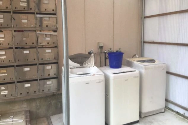 男子寮にある共用の洗濯機と集合ポストの画像。