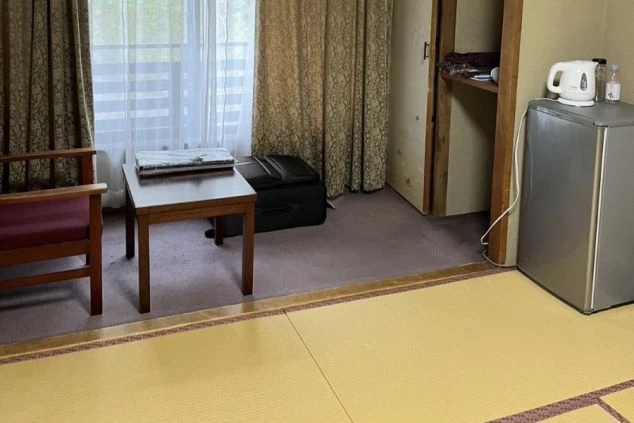リゾートバイトの寮の部屋。畳のスペースとカーペットのスペースがあり、テーブル、冷蔵庫、収納が備え付けられています。
