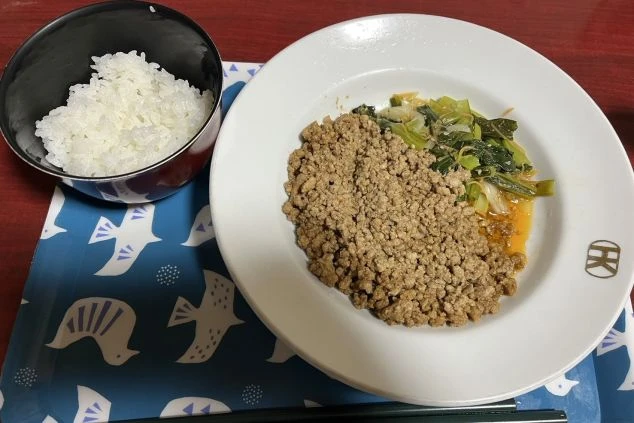 鶏ひき肉と野菜がのった料理と、ご飯が入った茶碗が写っている。
