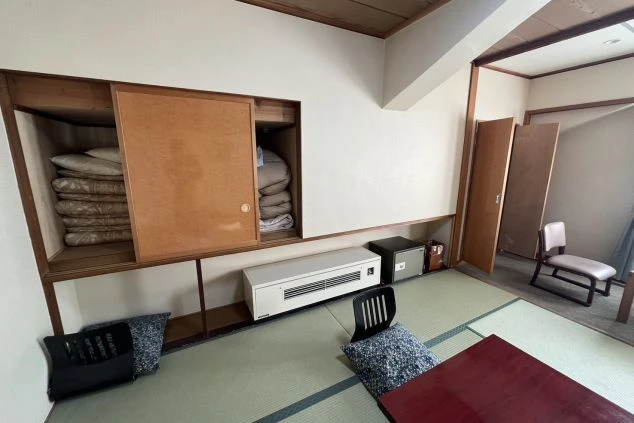 畳の床にある、布団が収納されたクローゼット。部屋には小さな冷蔵庫とヒーター、座布団が置かれている。