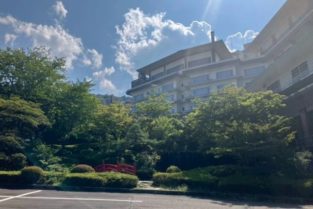 豊かな緑の庭園と赤い太鼓橋が美しい、伊香保温泉の大型旅館の外観と庭園の画像。