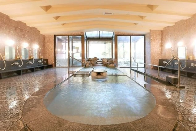 ホテルの広々とした大浴場。洗い場と窓から景色が見える湯船が映る職場のイメージ画像。