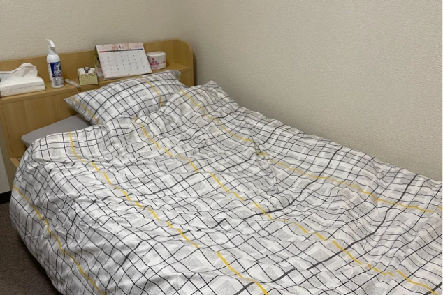 リゾートバイトの個室寮にあるシングルベッド。チェック柄の布団と枕が用意され、仕事の疲れを癒せる快適な寝室の画像。