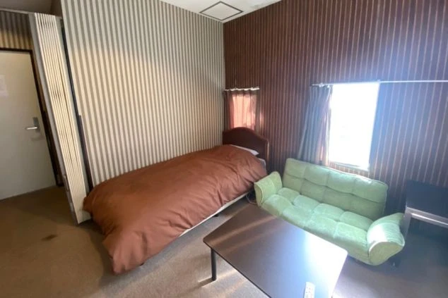 リゾートバイトの社員寮の部屋を表現するイメージ画像。ベッドやソファ、ハンガーラックが備え付けられたシンプルな個室。