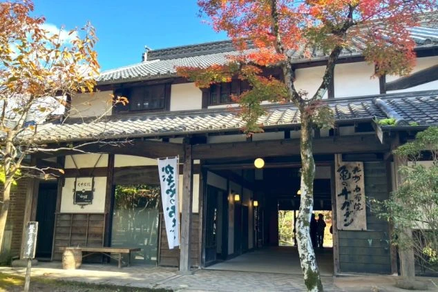 秋の紅葉に囲まれた日本の伝統的な旅館の外観。木造の建物と青空、鮮やかな赤やオレンジのモミジ。