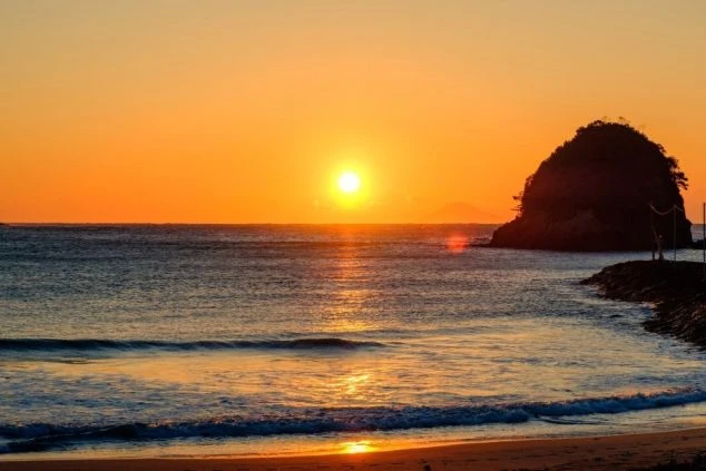 夕日が水平線に沈む伊豆の海岸。オレンジ色に輝く空と海が、ロマンチックな雰囲気を醸し出す。