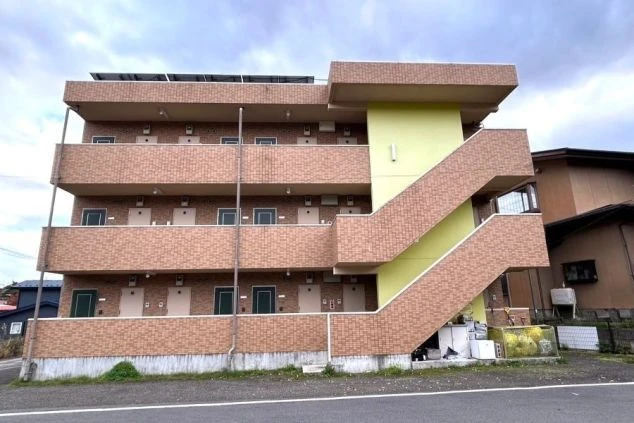 リゾートバイトの寮の外観の画像。レンガ調の壁と緑色の階段が特徴の複数階建てのアパートメント。