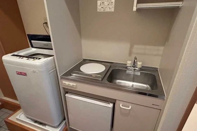 リゾートバイトの個室寮に完備されたミニキッチン。IHクッキングヒーター、シンク、小型冷蔵庫、さらに室内洗濯機がコンパクトにまとまった、自炊派に嬉しい便利な生活環境。