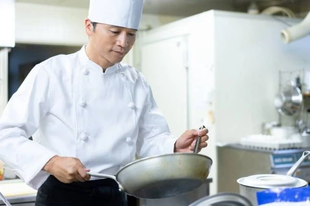 厨房でフライパンを使い調理をするシェフの姿が映るイメージ画像。リゾートバイトの調理業務の様子。