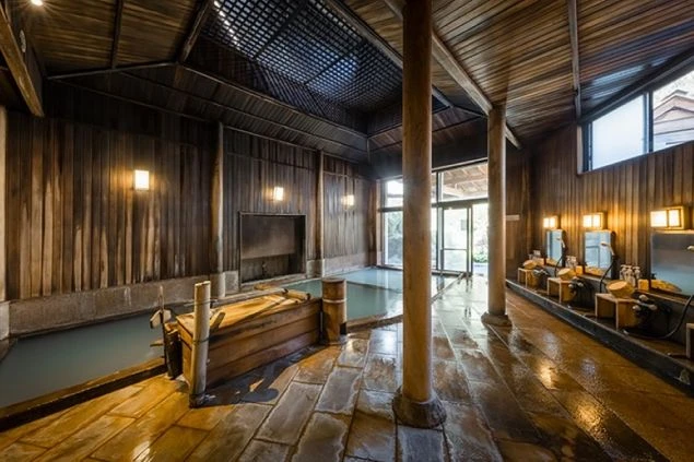 木造の広々とした大浴場。湯気が立ち上る湯船と洗い場、窓から光が差し込む温泉のイメージ画像。リゾートバイトの休日を満喫。