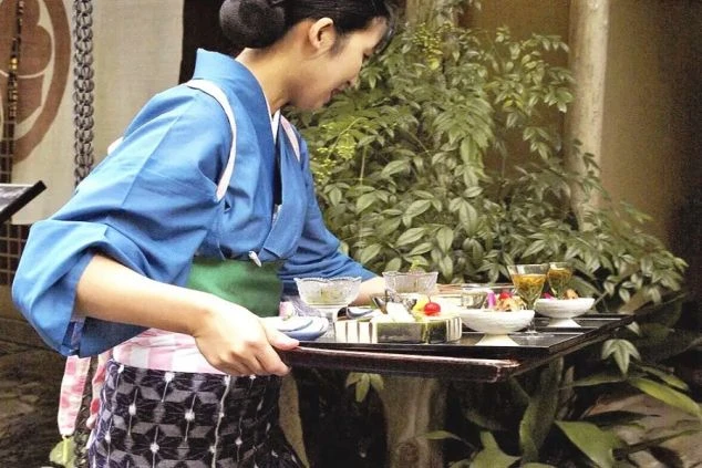 和食を運ぶ、作務衣を着た女性の画像。