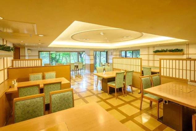 和モダンで清潔感のあるリゾートホテルのレストランの画像。窓から緑が見える明るい空間で、木のぬくもりを感じるテーブル席が並ぶ。