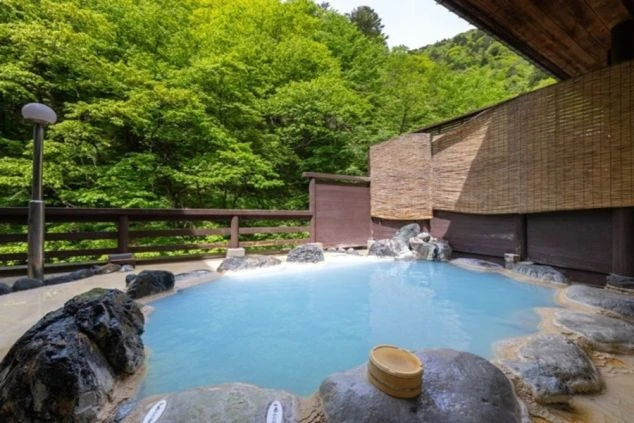 秋の夕暮れ、山麓に佇む風情ある温泉旅館の外観。白壁と木造の建物から温かい光が漏れ、旅情を誘う。