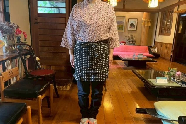 旅館の接客係の制服を着た人物の全身写真。