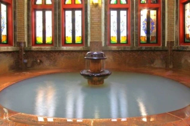 ステンドグラスの窓が特徴的な円形の温泉。湯気が立ち上る幻想的な浴槽が映るイメージ画像。リゾートバイトの休日を満喫。