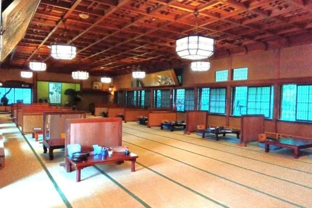 旅館の和風ダイニング。畳敷きの広間に低いテーブルと座布団、提灯が並ぶ職場のイメージ画像。