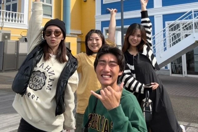 カラフルな建物を背景に、楽しそうにポーズをとる4人の写真。笑顔いっぱいで、仲の良さが伝わる集合写真。