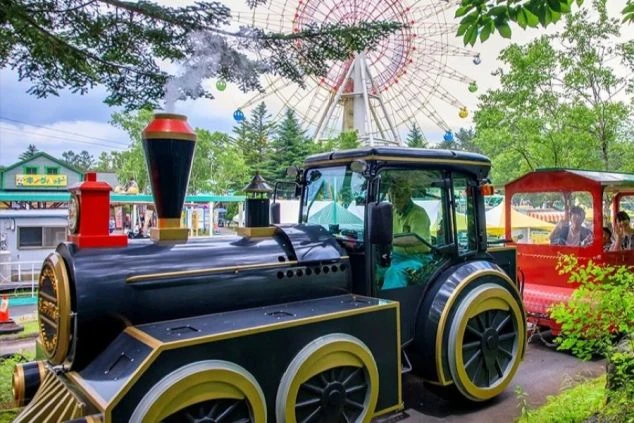 大きな観覧車を背景に、パーク内を走る蒸気機関車型のアトラクションの画像。