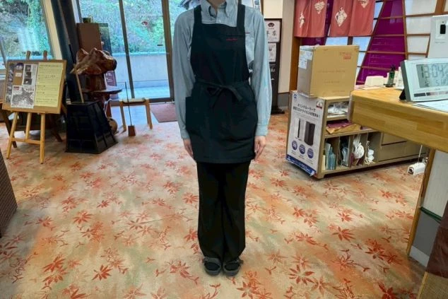 黒いエプロンとシャツ、パンツの旅館の制服。リゾートバイトで宿泊業務全般を担う女性の仕事着のイメージ。