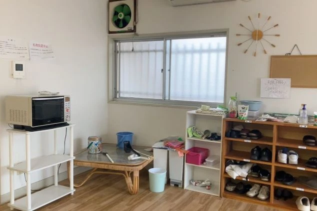 スタッフ寮の共有スペースの画像。電子レンジが置かれたラックや、整理整頓された下駄箱、掃除用具が備え付けられたフローリングの共用エリア。