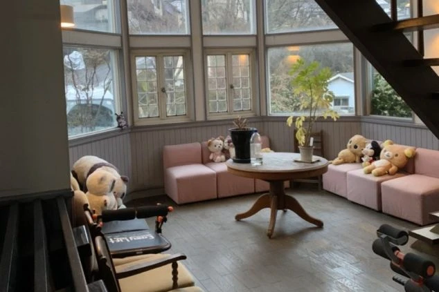 窓が大きく、ぬいぐるみが置かれたピンクのソファと丸いテーブルがある、明るいサンルームのような休憩スペース。